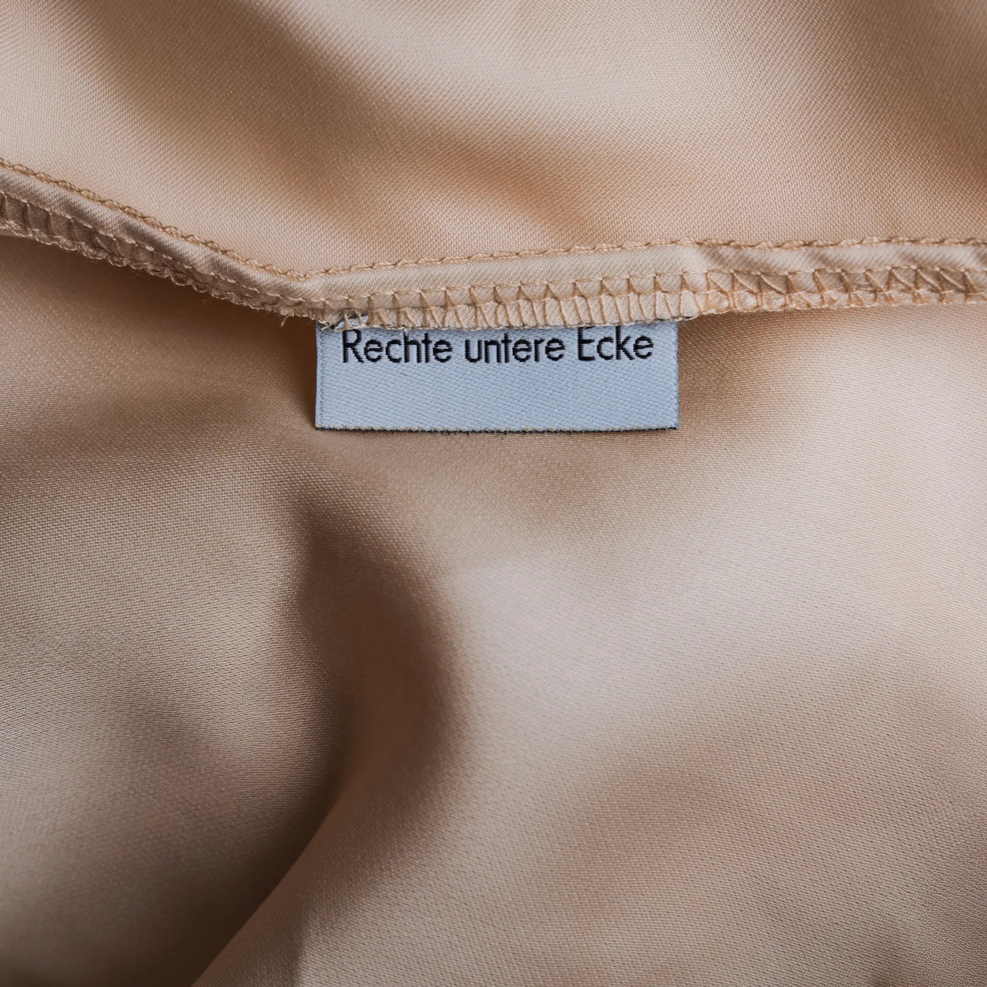 Beiges Spannbettlaken aus Micro TENCEL™ Lyocell „Shell Dune“, Detailansicht der rechten unteren Ecke mit eingenähtem Label, seidige Oberfläche und luxuriöse 400 TC Qualität
