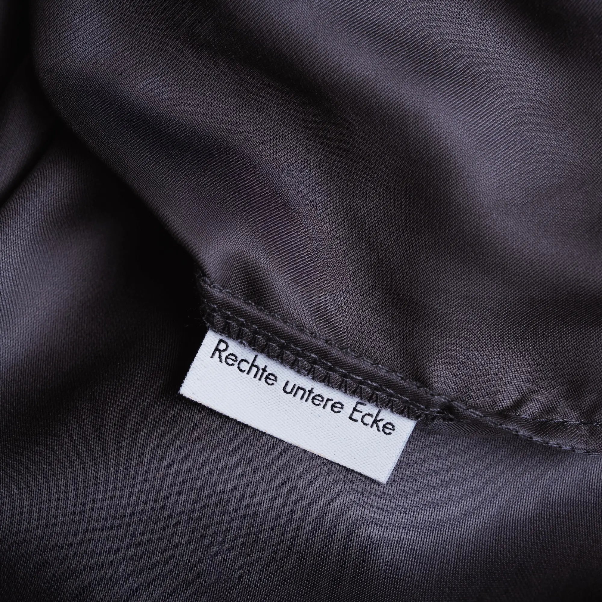 Dunkelgraues Spannbettlaken aus Micro TENCEL™ Lyocell, Detailansicht rechte untere Ecke mit eingenähtem Orientierungsetikett