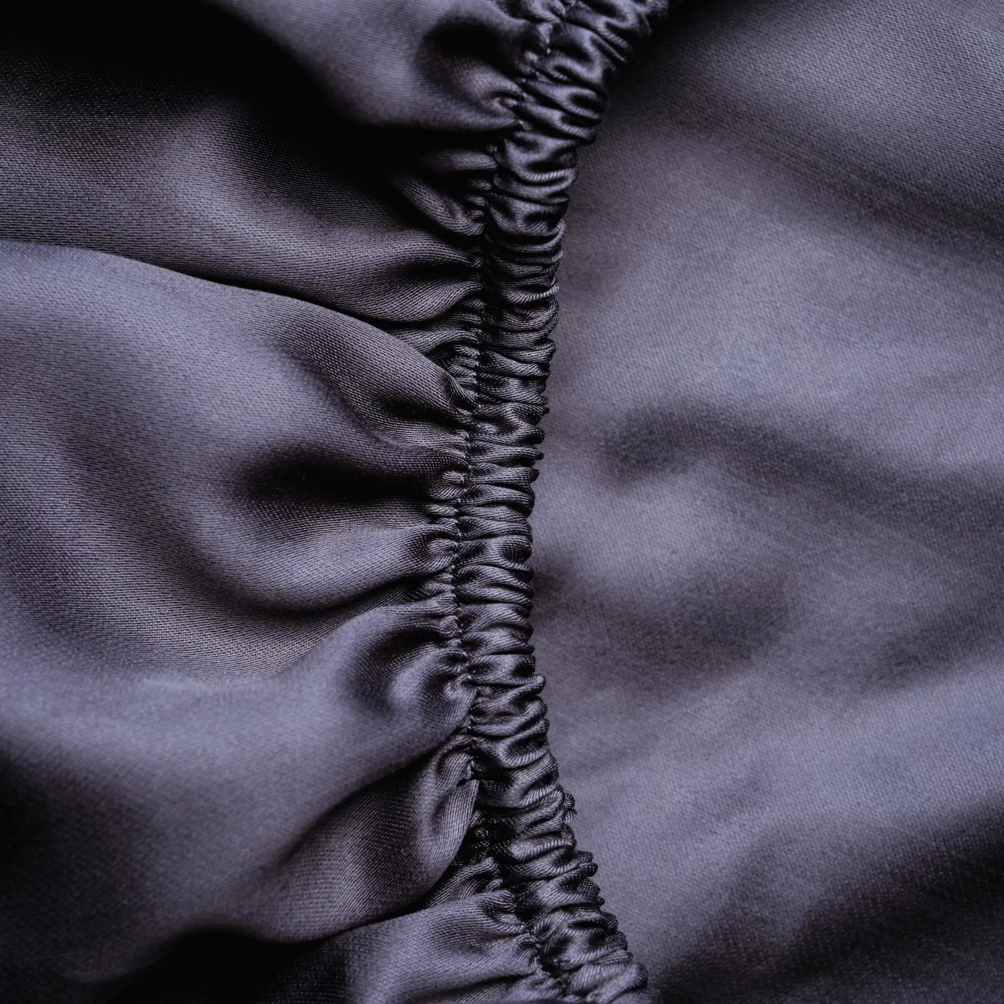 Dunkelgraues Spannbettlaken aus Micro TENCEL™ Lyocell, Nahaufnahme des Rundumgummis, seidig-glatt, atmungsaktiv und temperaturregulierend