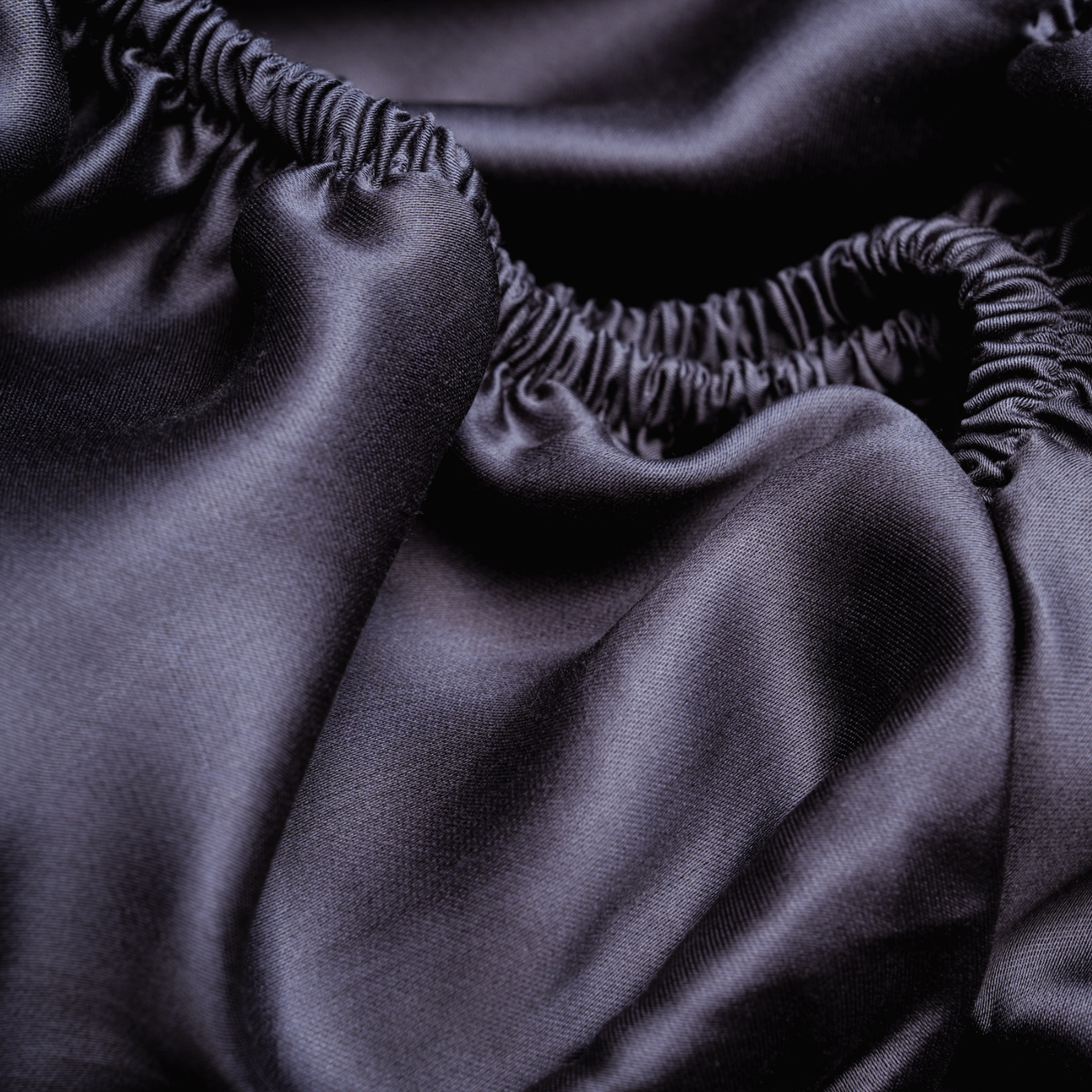 Detailaufnahme eines dunklen Lyocell-Spannbettlakens mit elastischem Bund – glatte, temperaturregulierende Bettwäsche.