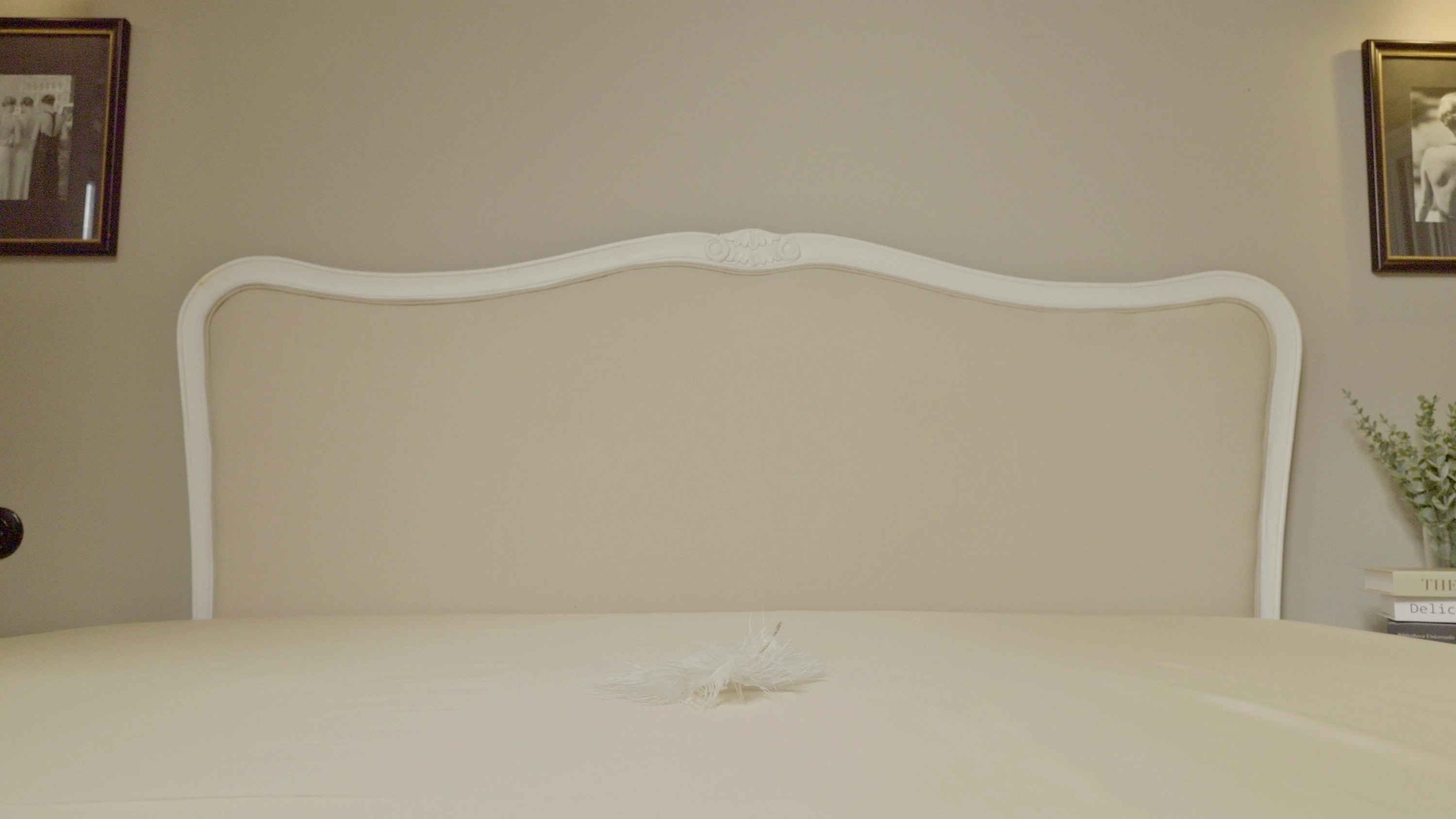 Nahaufnahme eines Bettes mit elegantem, weiß gerahmtem Kopfteil und beigefarbenem Spannbettlaken aus TENCEL™ Lyocell – stilvoll dekoriert für nachhaltigen, luxuriösen Schlafkomfort