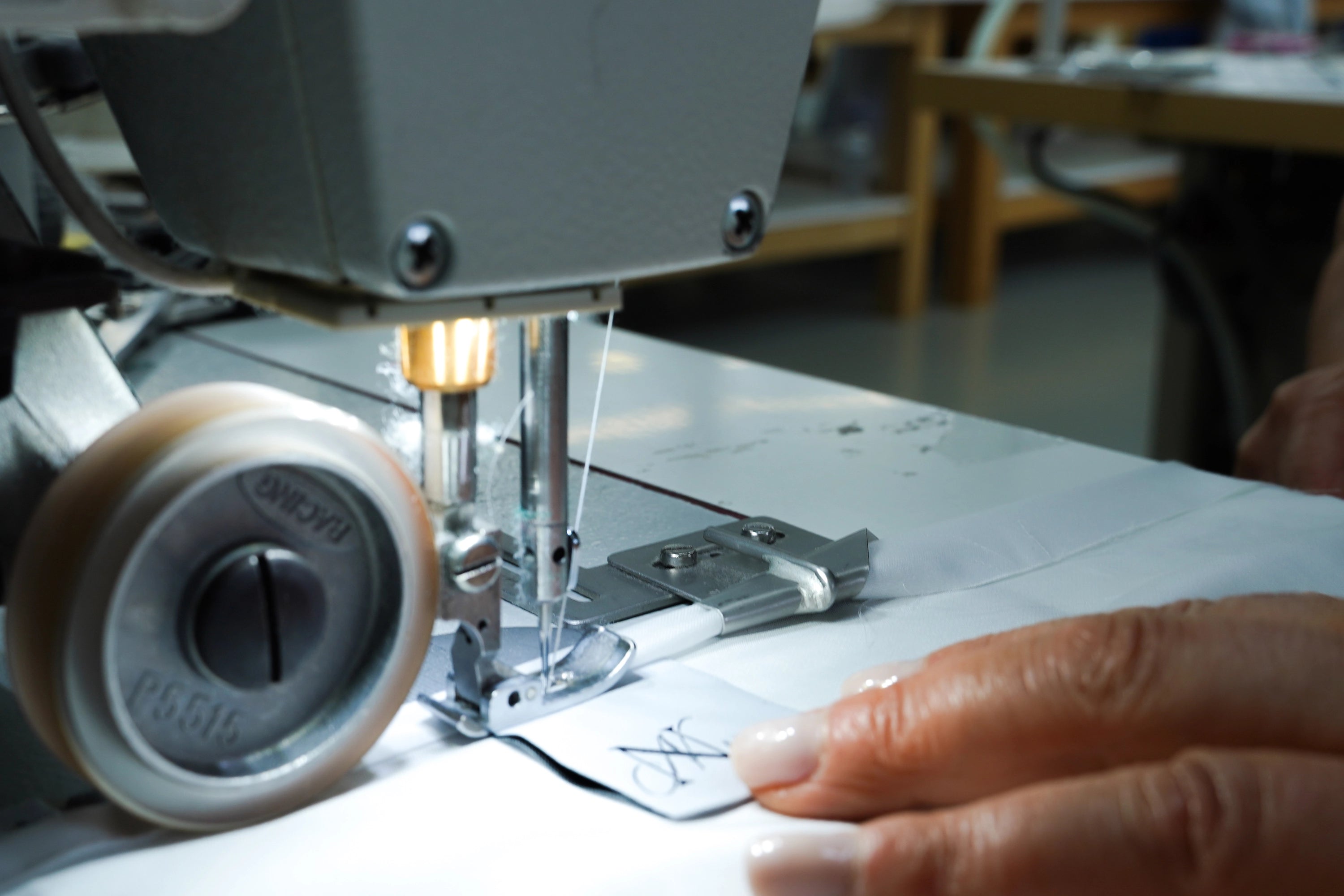 Detailaufnahme einer Nähmaschine, die ein Markenlabel in ein weißes Spannbettlaken aus TENCEL™ Lyocell einnäht – Symbol für präzise Handarbeit und nachhaltige Herstellung