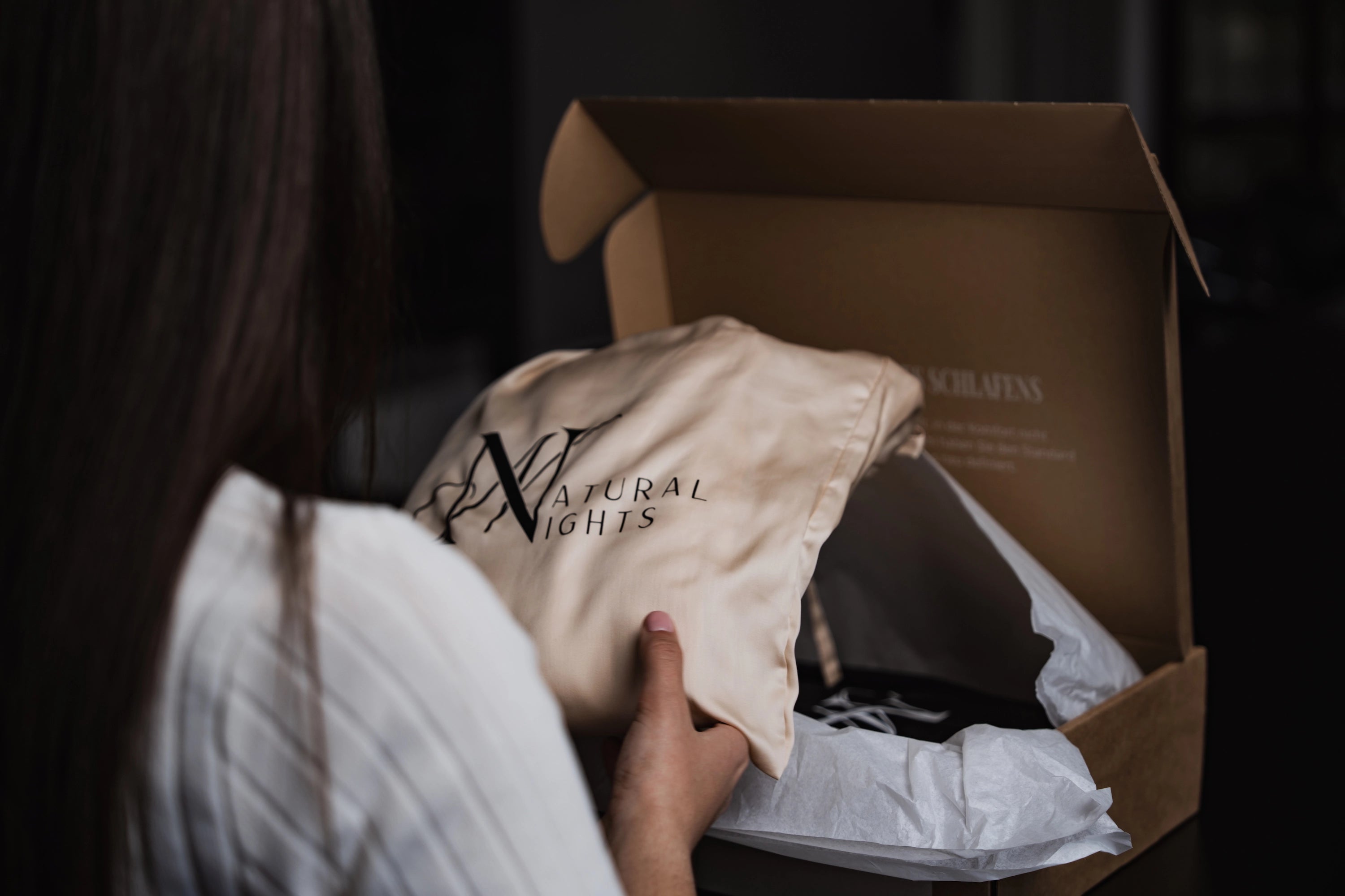 Frau packt beiges TENCEL™ Lyocell Spannbettlaken aus Natural Nights Box aus, edle und nachhaltige Premiumbettwäsche.